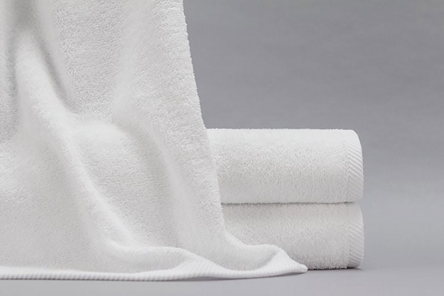 A Gradient bath towel draped over a stack of two folded Gradient bath towels.