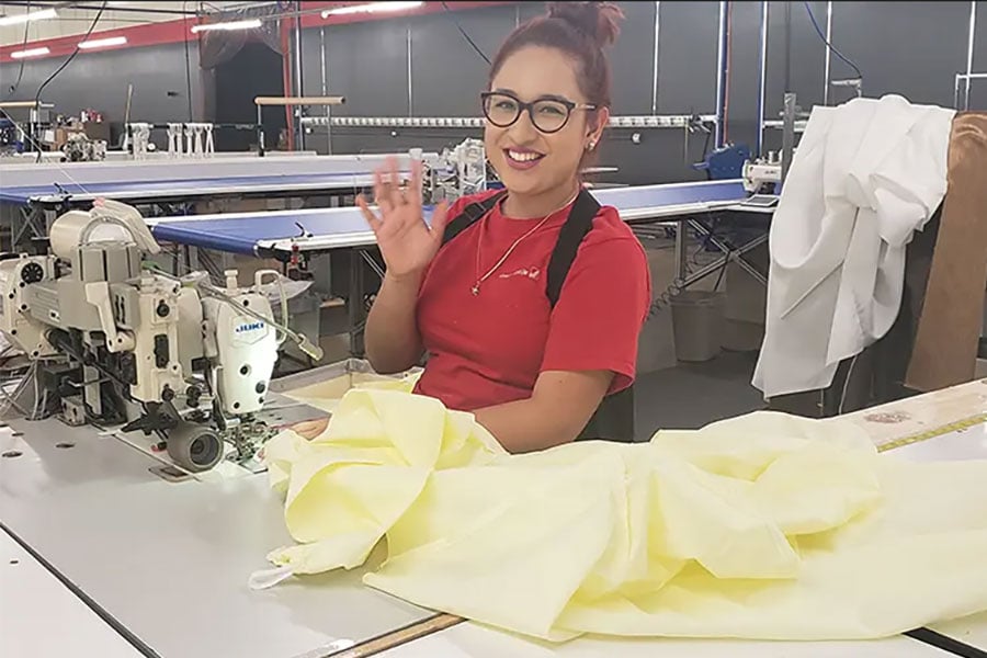 Person at a sewing machine in a factory waving with fabric on the table.