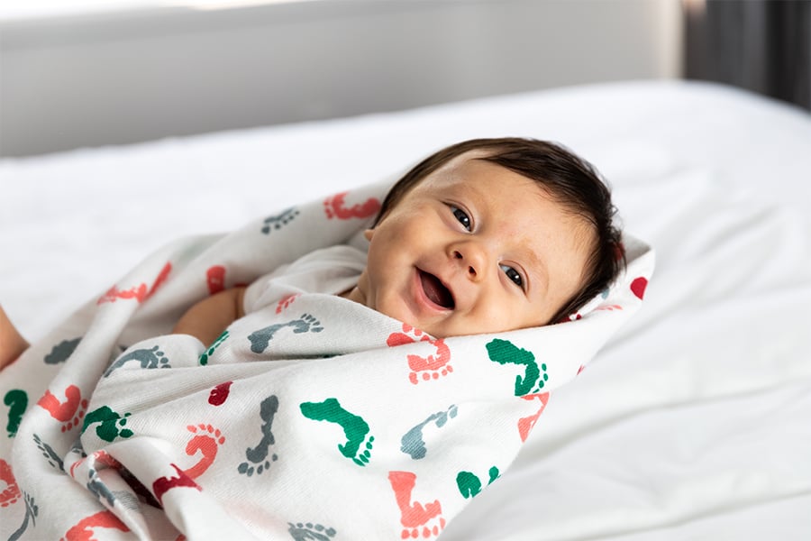 Baby wrapped in a patterned blanket lying on a bed.