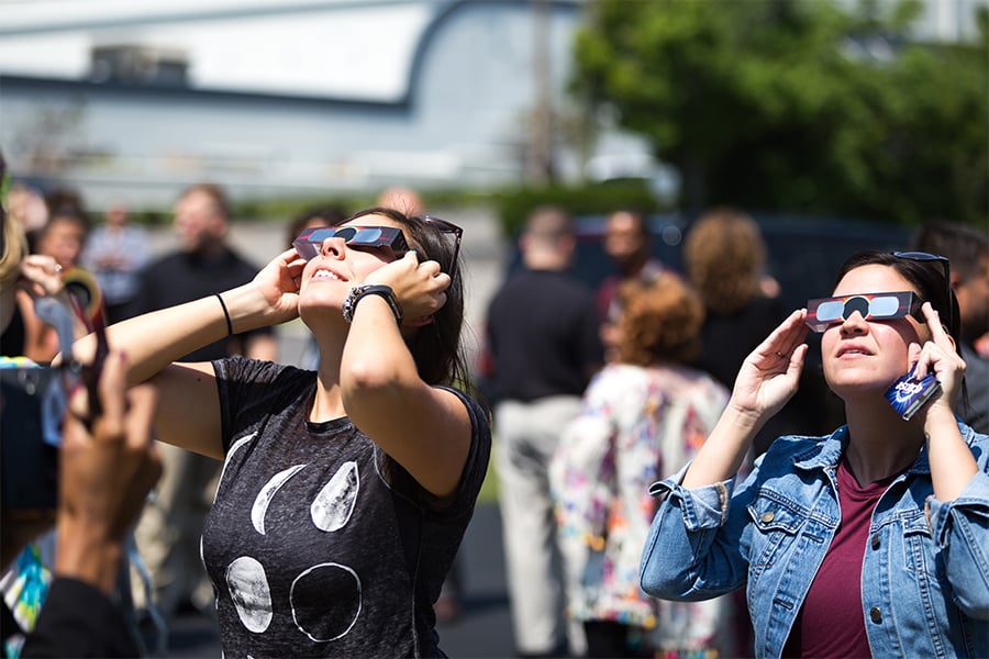 People outdoors wearing eclipse glasses and looking up at the sky.
