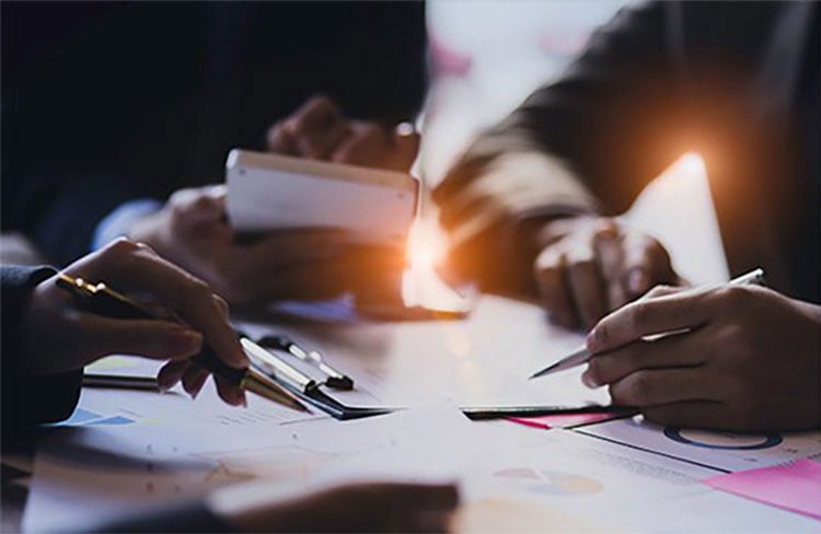 Hands collaborating over documents with pens and a smartphone on a table.