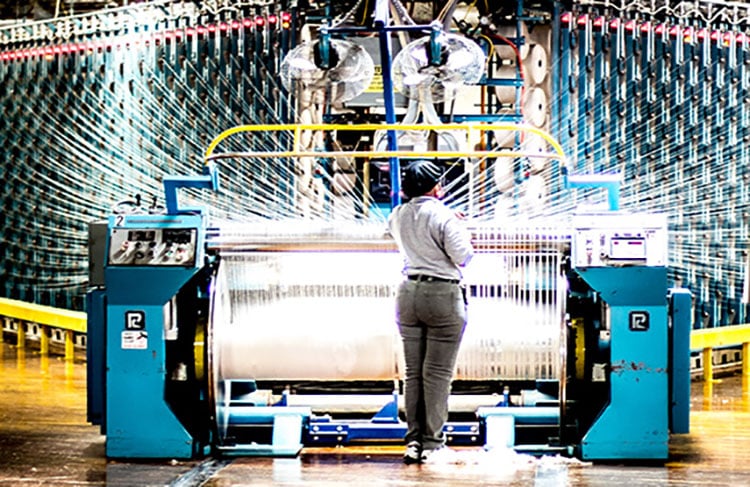Person standing at industrial loom with multiple threads in a textile factory.