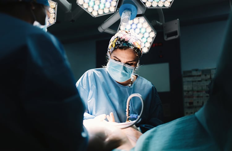 Surgical procedure being performed in an operating room under bright lights.