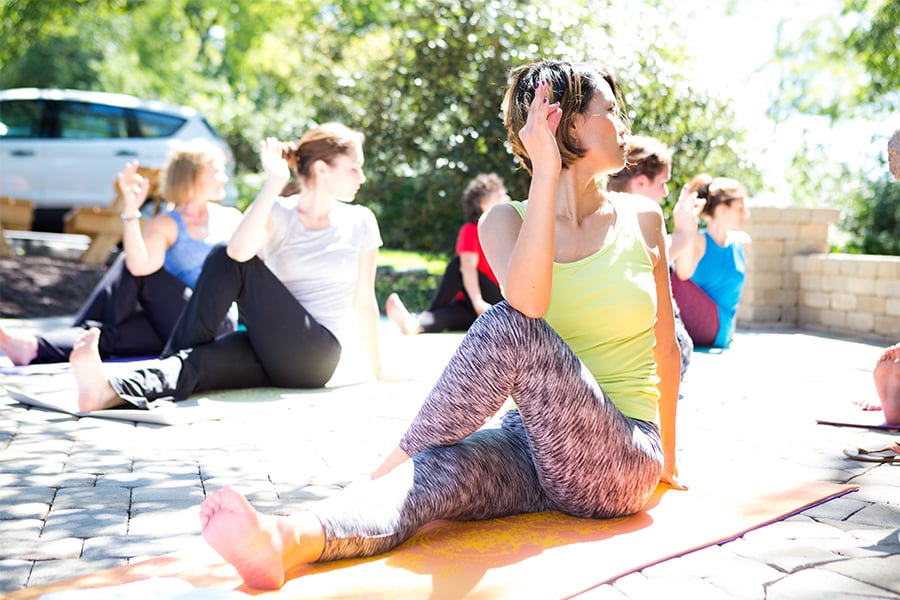 People sitting on mats outdoors performing a seated twist yoga stretch.