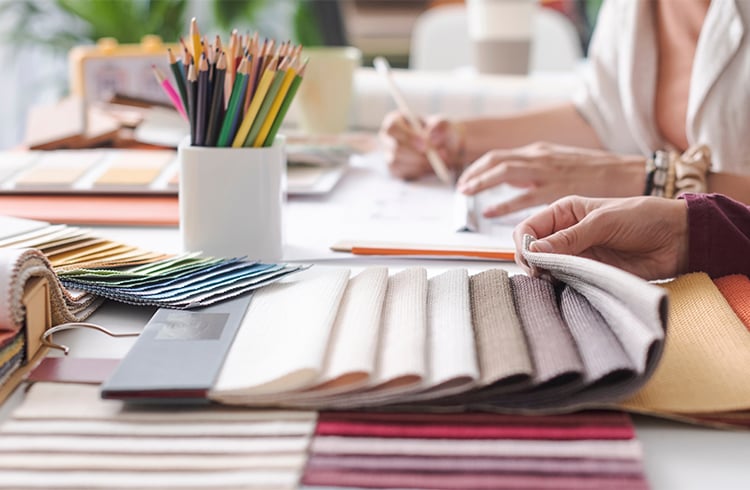 Interior Designers are comparing fabric swatches. A white vase contains many colorful pencils.