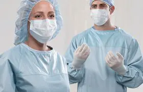 Two doctors prepping for surgery, wearing surgical gowns, masks, gloves, and hair protection.