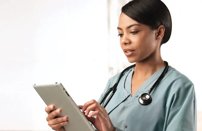 Nurse with Stethoscope consulting patient files on tablet.