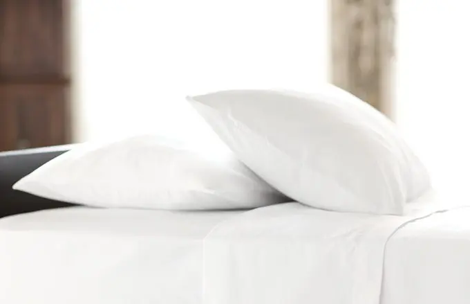 two fluffy chamber pillows laying on a hotel room bed with window in the background