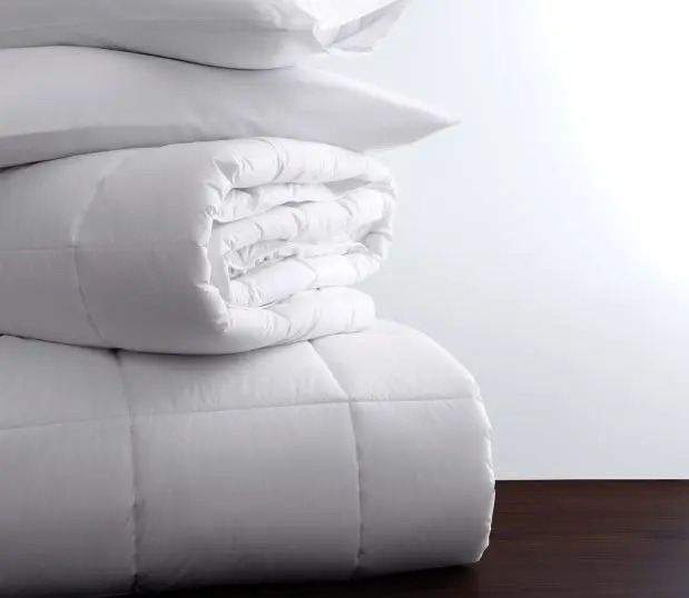 A stack of white bedding featuring Luxsoft a luxury comforter. This comforter is filled with a 100% Recycled Down Alternative.