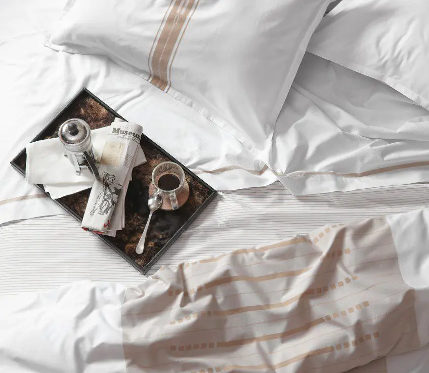 Messy bed with luxury hotel sheets and a breakfast tray.
