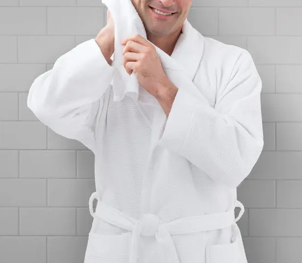 A photo of a man wearing a white, honeycomb bathrobe. He is rubbing his head with a towel suggesting he just got out of a shower.