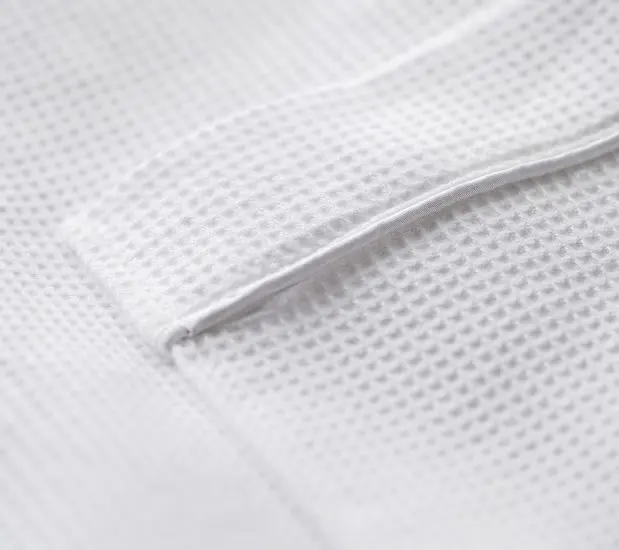 Detail of the pocket of the spa Waffle bathrobe. The familiar waffle weave design is complemented with white satin piping.