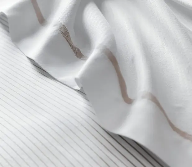 Detail of Concerto Sheeting. The fitted sheet has fine beige lines and the top sheet has one beige stripe along the top hem.