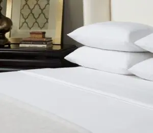White luxury hotel sheets shown on a boutique hotel bed with a white leather headboard.