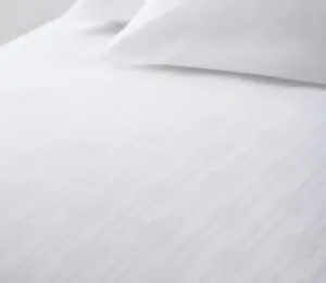 Image of the White Reed Top Cover on a bed with a couple of white pillows. This top sheet has a subtle stripe and square design. A top cover is more easily laundered than a bedspread and will make for a more sanitary and hygienic room.