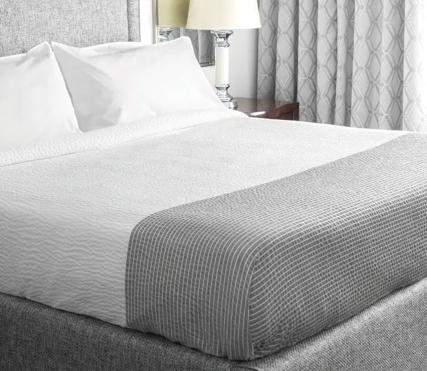 Cumulus StormCloud shown on a hotel bed with a gey linen headboard. StormCloud differs from regular Cumulus because of the grey band at the foot of the bed that helps disguise dirt from heavy use.