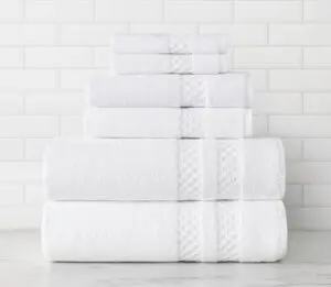 This is a stack of white luxury bath towels, hand towels and wash towels. The dobby bands near the hems feature a raised square pattern.