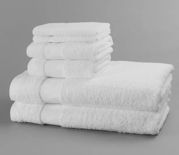 Two each of white absorbent bath towels, hand towels and washcloths stacked and shot against a grey backgrouond.