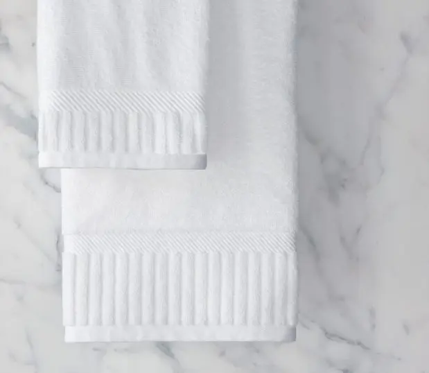 The Piano Key collection features 100% cotton hotel towels with an elegant dobby border. The sophisticated look is finished with distinctive piano key end panels. Show here: a hanging bath and hand piano key towel in front of a marble background.
