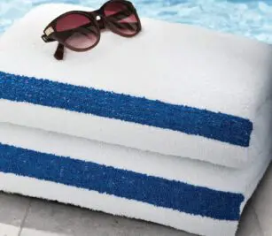 Sunglasses on top of a stack of white towel with a blue stripe. These pool towels in bulk are perfect for budget minded properties.
