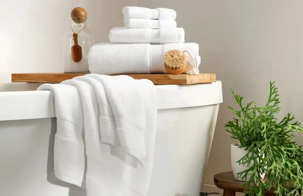 Lynova® uses luxurious, low twist microcotton to create the softest towels in hospitality. Image shows a stack of 100% cotton towels in a bathroom setting.