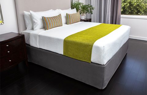 A hotel bed featuring decorative pillows and a green bed scarf.