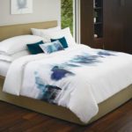 A well-made hotel bed featuring a custom printed duvet cover and decorative throw pillows.