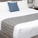 A stylishly made hotel bed featuring decorative pillows and a decorative bed scarf.