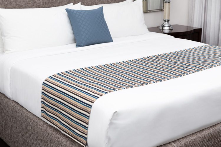 A stylishly made hotel bed featuring decorative pillows and a decorative bed scarf.