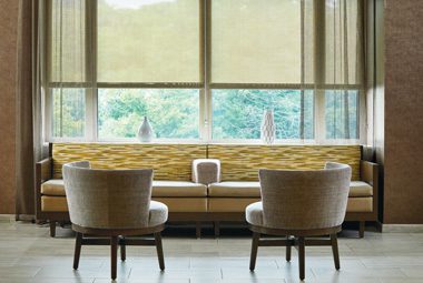 Two modern style chairs facing a long yellow couch in front of a large window.