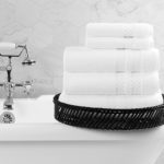 A stack of folded Capitol Bath Towels and Wash Cloths rest on the edge of an classic style clawfoot bath tub.