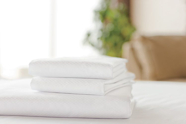 A stack of folded white Centium Satin sheets rest on a bed.