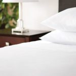 A hotel bed next to nightstand with Centium Satin sheets and two pillows.