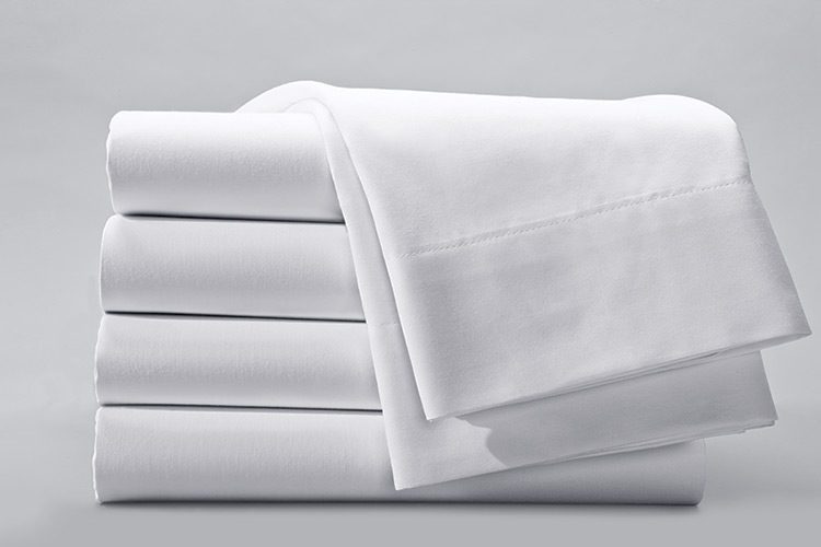 A stack of folded bed sheets, an additional folded sheets is draped over the top of the stack.