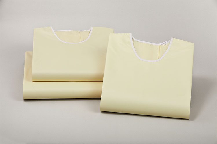 A folded ComPel Precaution gown leaning agains a stack of two additional folded gowns.