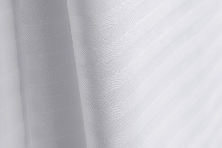 Close up image of ComforTwill hotel sheets in tone-on-tone white stripe