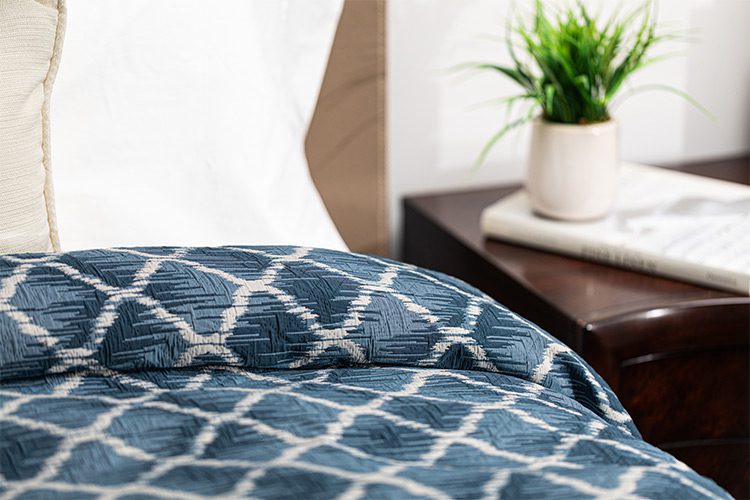 The image is of a dark blue custom healthcare bedspread with a criss-cross design. The fabric is called Melrose.