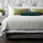 A well-made hotel bed featuring two Limelight throw pillows and a Eucalyptus bolster pillow.