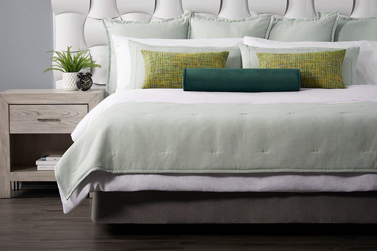 A well-made hotel bed featuring two Limelight throw pillows and a Eucalyptus bolster pillow.