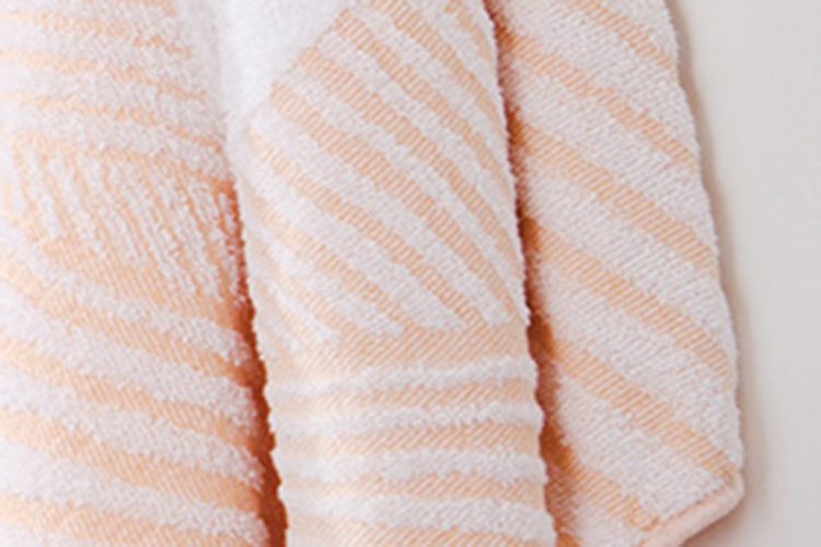 Image of a hanging towel. It is an Elevations towel with an abstract pattern in the color of creamsicle.