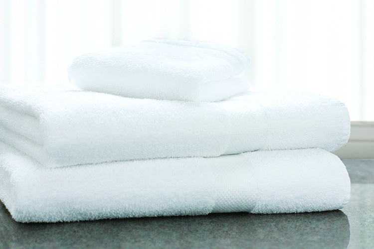 A stack of EuroClassique bath towels and a washcloth sit atop a marble countertop.