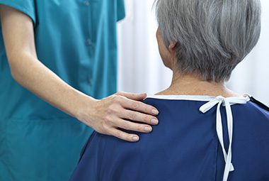 A nurse's hand rests on a patient's shoulder.