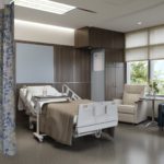 A healthcare patient room featuring privacy curtains, a patient bed, a chair, and a sofa.