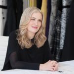 Designer Heidi Weisel poses in front of a wall of various fabrics and patterns.