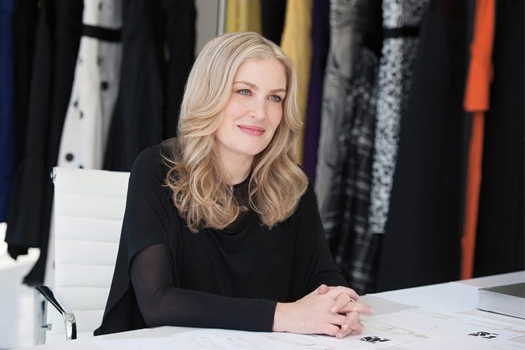 Designer Heidi Weisel poses in front of a wall of various fabrics and patterns.