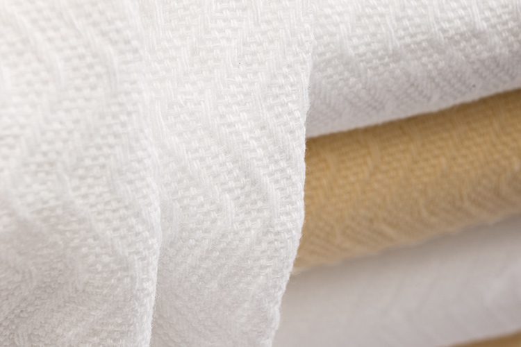 Detail of a stack of herringbone blankets in bleached and natural.