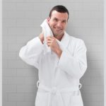 A man is wearing a honey comb bath robe and drying his face with a white hotel towel.