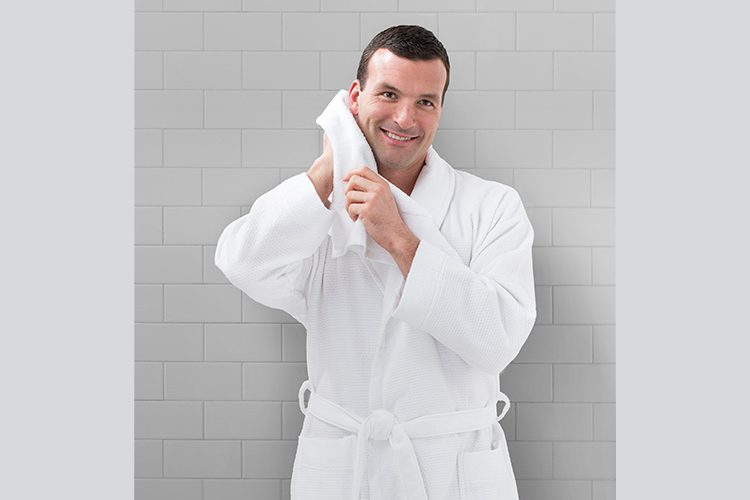 A man is wearing a honey comb bath robe and drying his face with a white hotel towel.