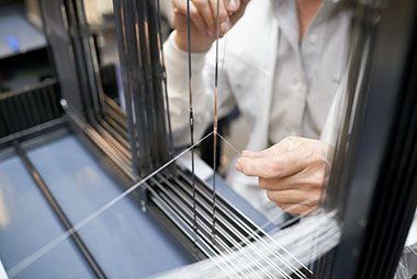 A close up image of a Standard Textile team member threading yarn onto a weaving machine.