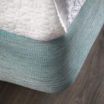 A close up image of the corner of a hotel bed featuring a Pivot/Tourmaline box spring cover.